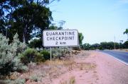 White sign with the words quarantine checkpoint 2km written in black. This sign is on the left hand side of a road.