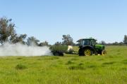 Fertiliser being spread on pasture from the trailer of a tractor - side view
