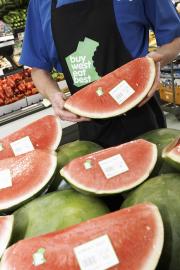 Greengrocer holding a sliced watermelon with Buy West Eat Best logo visible on packaging.