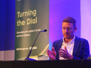 Adam Carrel seated on stage with a Turning the Dial banner in the background