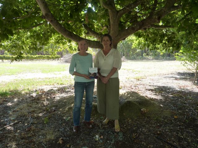 Two women standing under a European tree, holding a copy of the Australian Truffle Orchards – Pest and disease field guide.