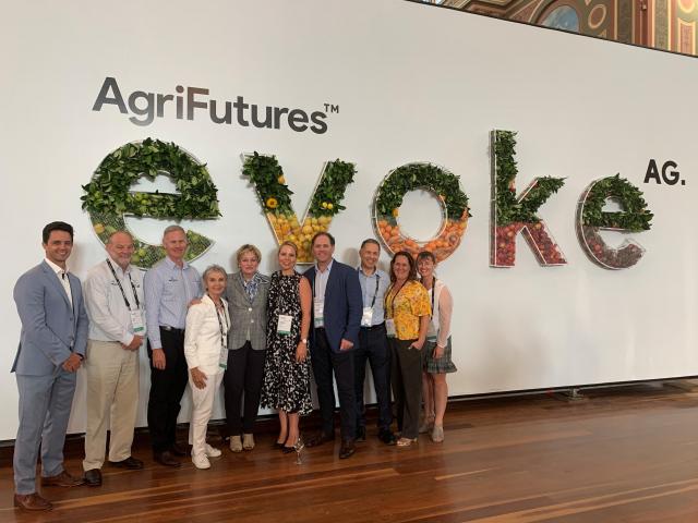Conference delegates stand in front of a sign made of fruits and foliage that says "Agrifutures evokeAG"