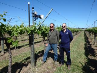 Two men in a vineyard standing next to a weather station. Two men in a vineyard standing next to a weather station.