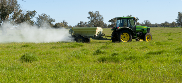 Fertiliser being spread on pasture from the trailer of a tractor - side view