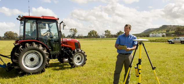 Research officer in fiield with GPS equipment next to tractor.