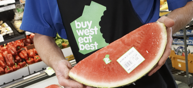 Greengrocer holding a sliced watermelon with Buy West Eat Best logo visible on packaging.