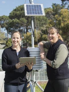 Two women leaning on a weather station