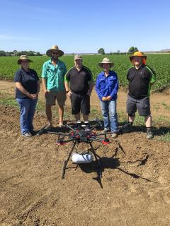 A group of people standing behind a drone in a paddock.