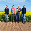Four people standing in front of a canola trial in full flower