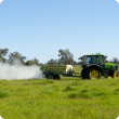 Fertiliser being spread on pasture from the trailer of a tractor - side view